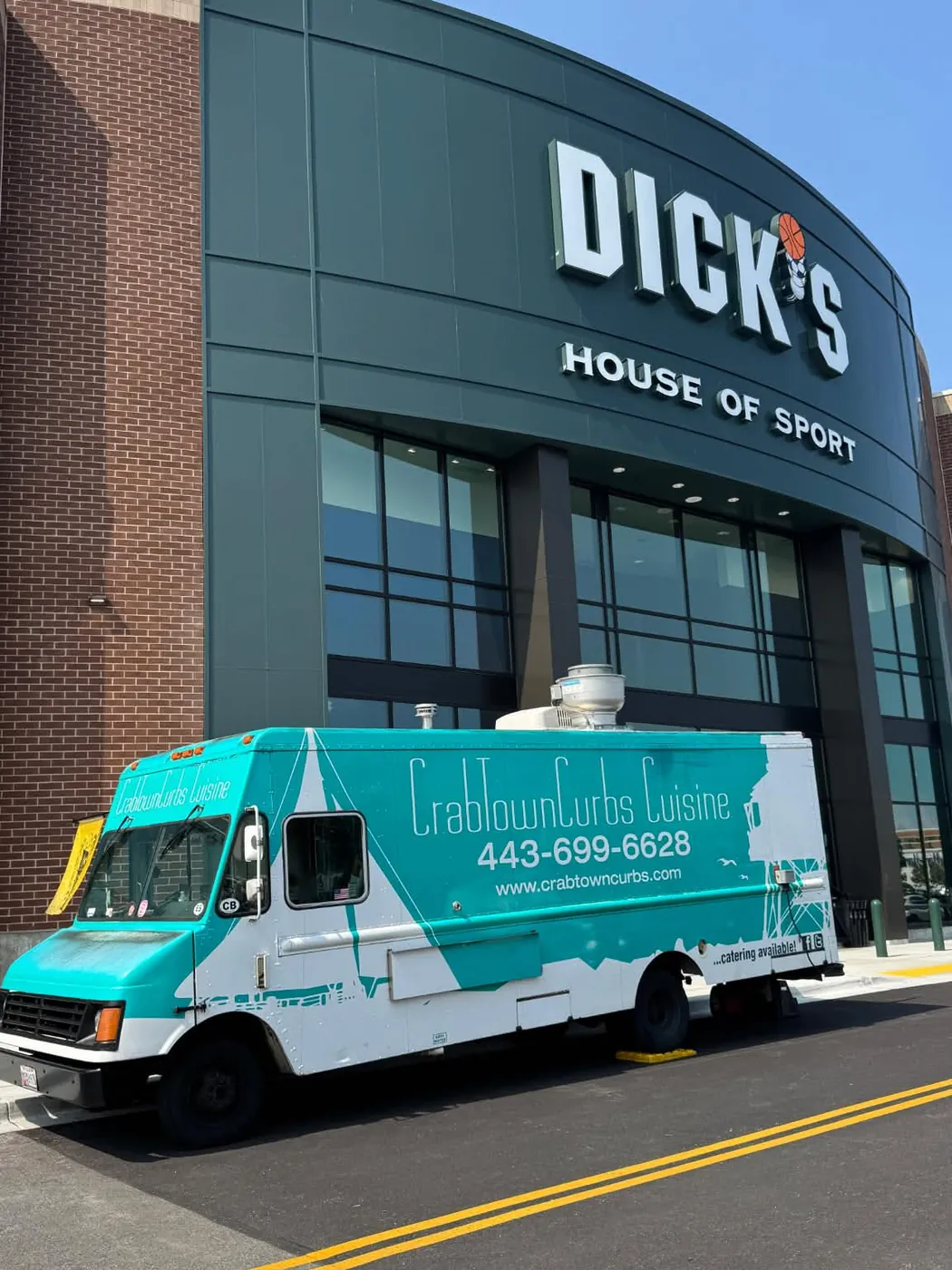 The teal CrabTown Curbs truck parked at the curb outside a DICK'S House of Sport store on a clear day.