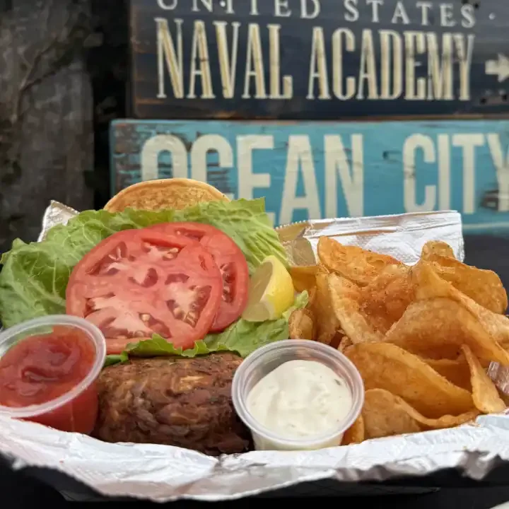 Crab cake sandwich with lettuce, tomato, lemon wedge, and homemade chips.